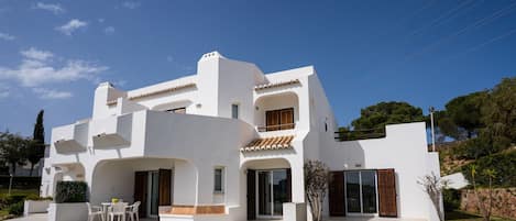 A modern white villa with a patio, outdoor seating, and a view of the surrounding landscape.