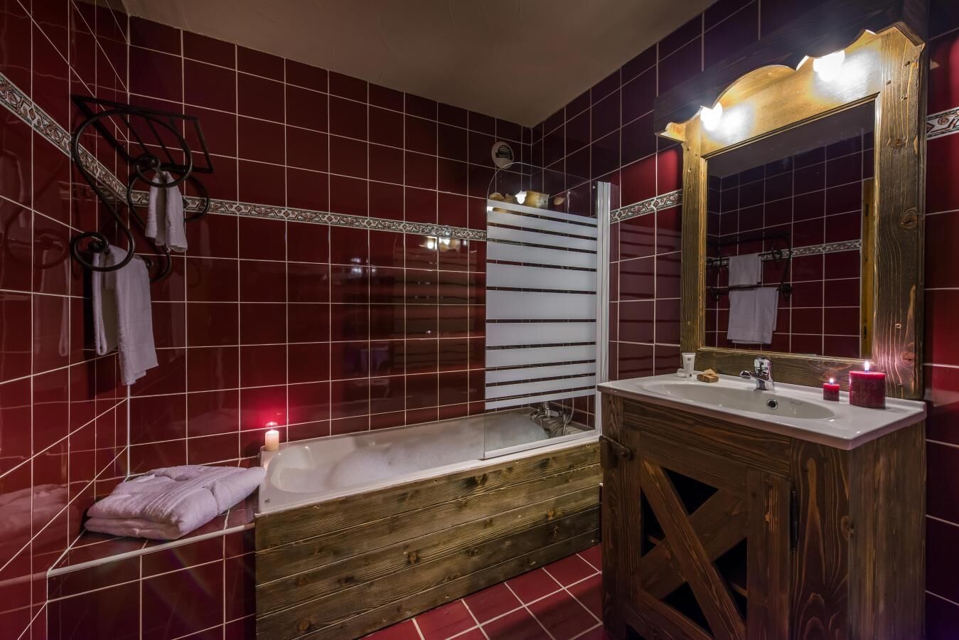 A bathroom with a wooden bathtub, a vanity with a mirror, and red tiled walls.