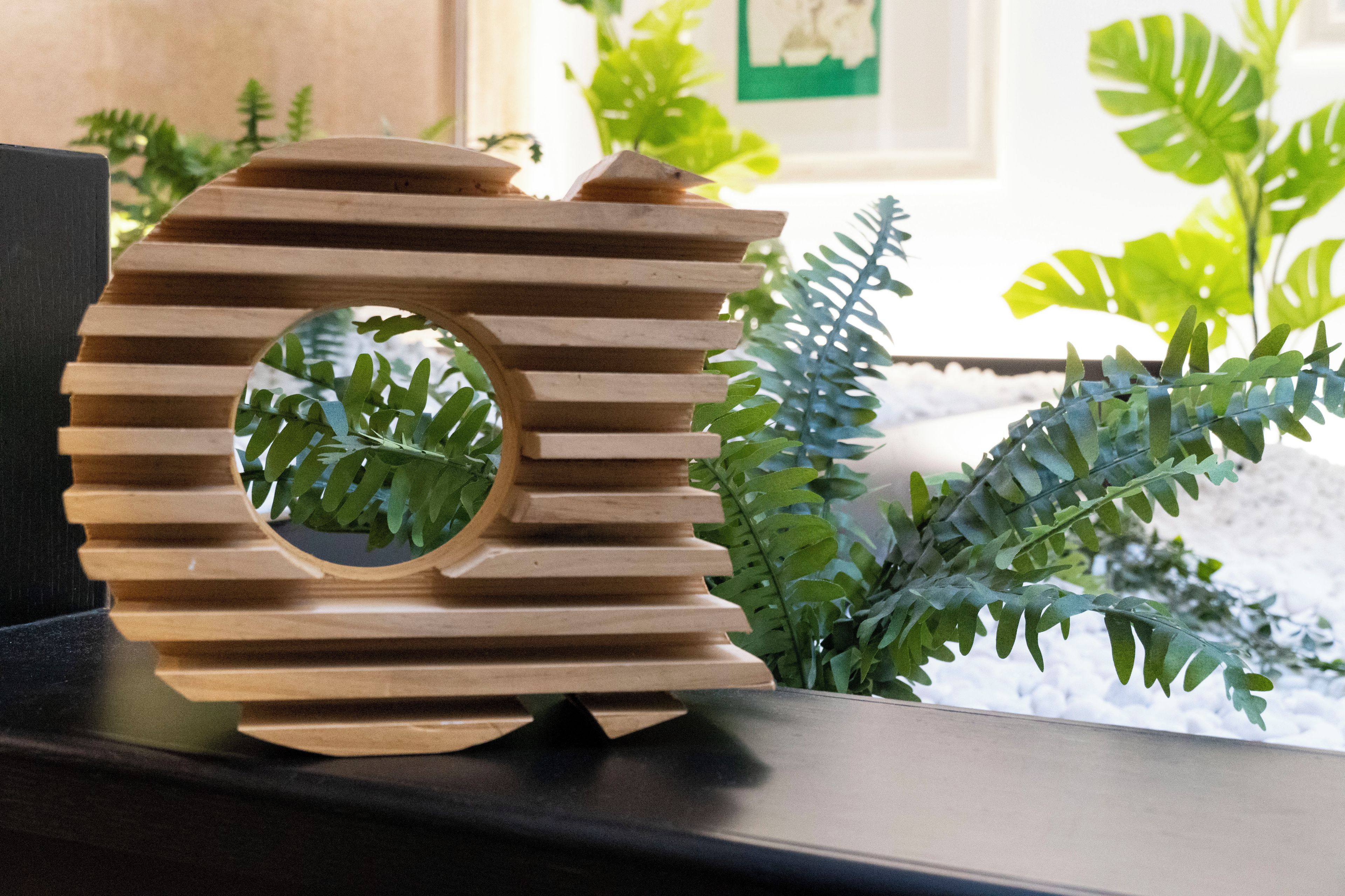 Un élément décoratif en bois, de forme circulaire et ajourée, posé sur une surface sombre, avec un feuillage verdoyant en arrière-plan.