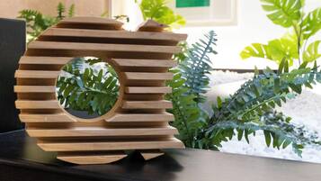 Un élément décoratif en bois, de forme circulaire et ajourée, posé sur une surface sombre, avec un feuillage verdoyant en arrière-plan.
