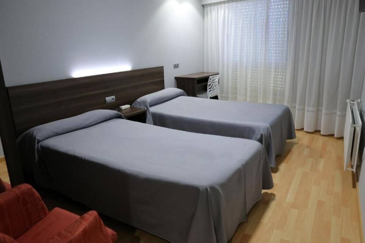 A hotel room with two beds, a desk, a chair, and a window with curtains.