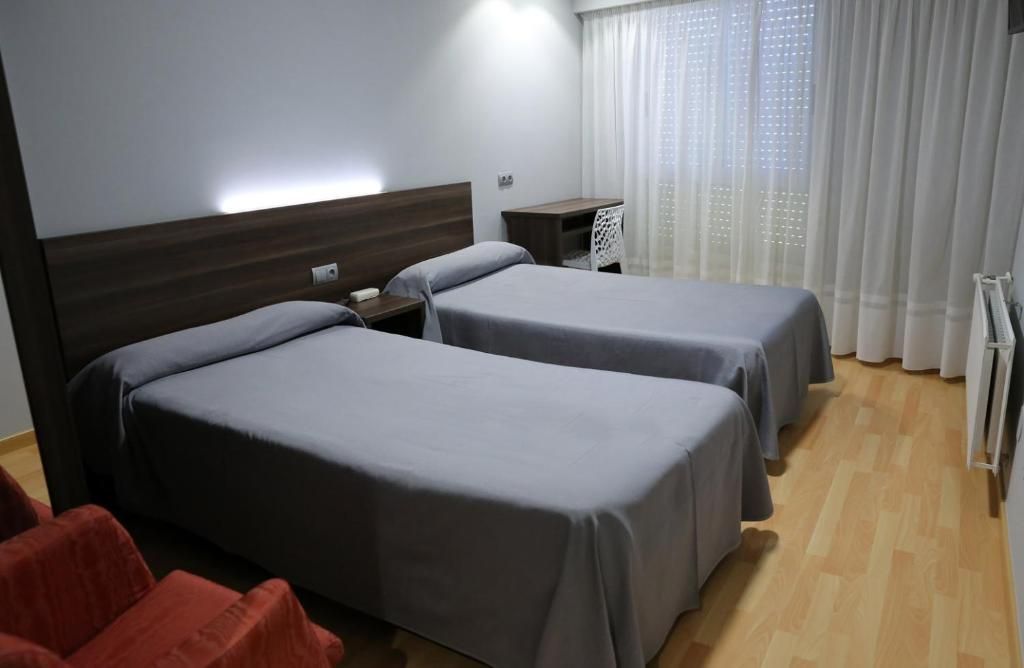 Une chambre d’hôtel avec deux lits, un bureau, une chaise et une fenêtre avec des rideaux.