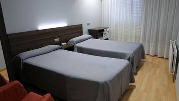 Une chambre d’hôtel avec deux lits, un bureau, une chaise et une fenêtre avec des rideaux.