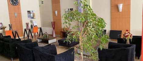 Un área de recepción con un reloj, asientos y una planta en maceta.