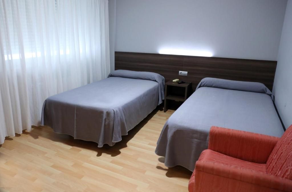 A hotel room with two single beds, a wooden floor, a nightstand with a phone, and a red chair.