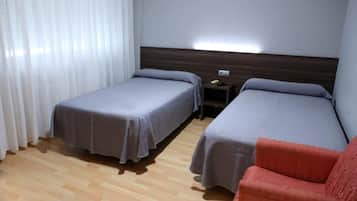 Habitación de hotel con dos camas individuales, suelo de madera, mesita de noche con teléfono y una silla roja.