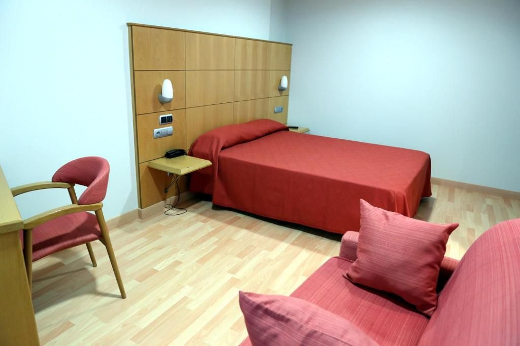 A small, neatly arranged room with a single bed, a desk, and a chair.