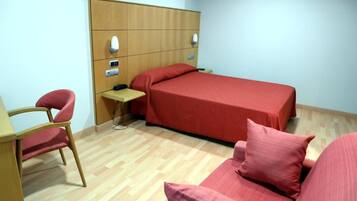 A small, neatly arranged room with a single bed, a desk, and a chair.