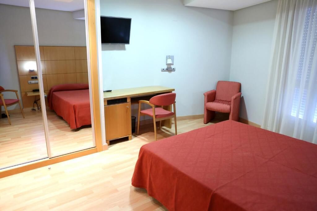 A hotel room with a bed, a desk, two chairs, a TV, and a mirror.