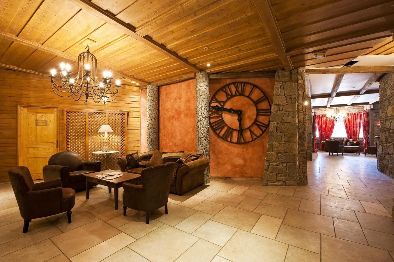 A cozy lobby with a large wall clock, wooden furniture, and a chandelier.