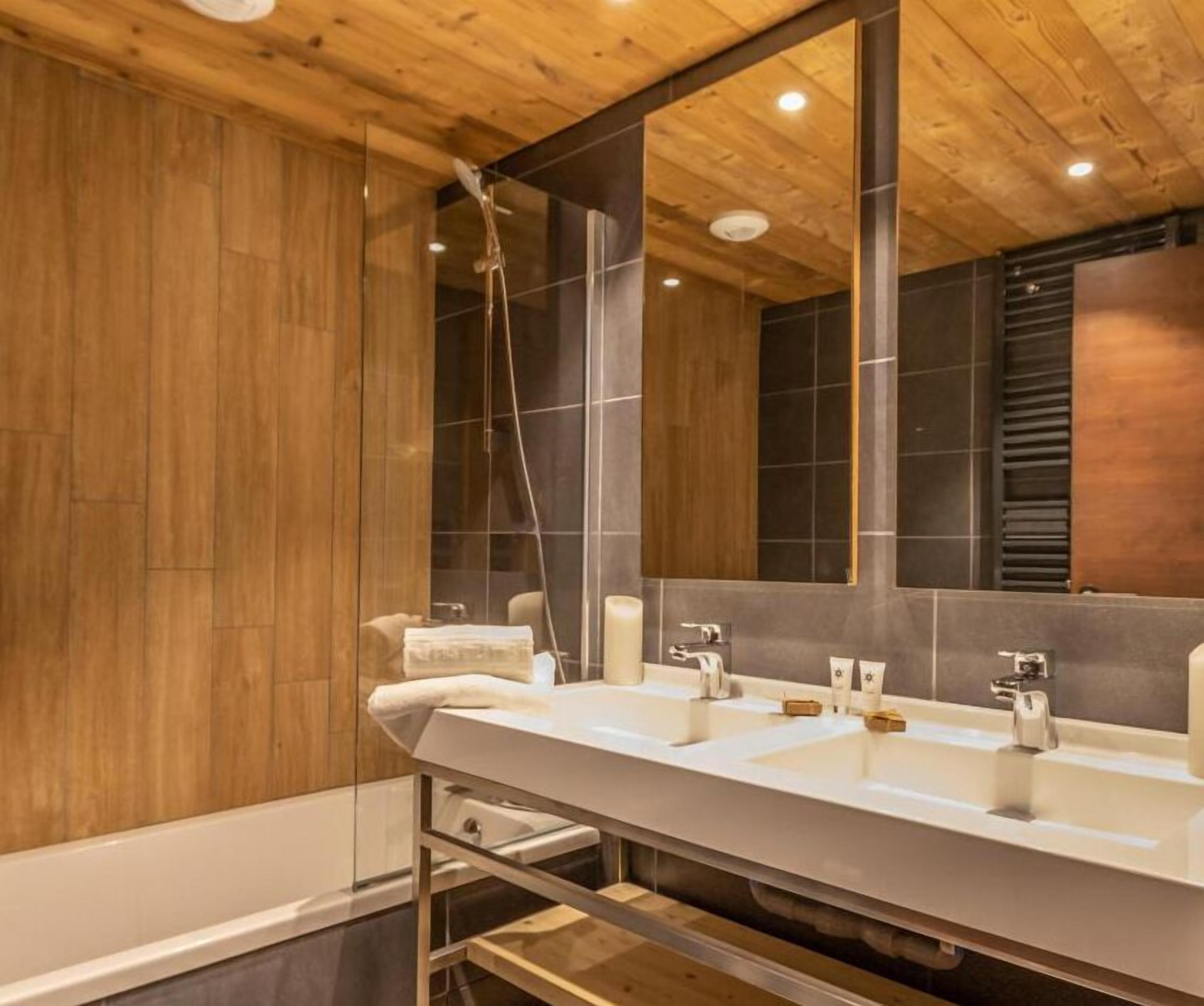 A modern bathroom with wooden ceiling, a large mirror, and a white sink with two faucets.