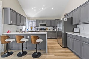 A modern kitchen with grey cabinets, a central island with bar stools, and a stainless steel refrigerator. - Sparkling SaltwtrPool•Spa•Firepit•Netflix•NFL+ (Phoenix)