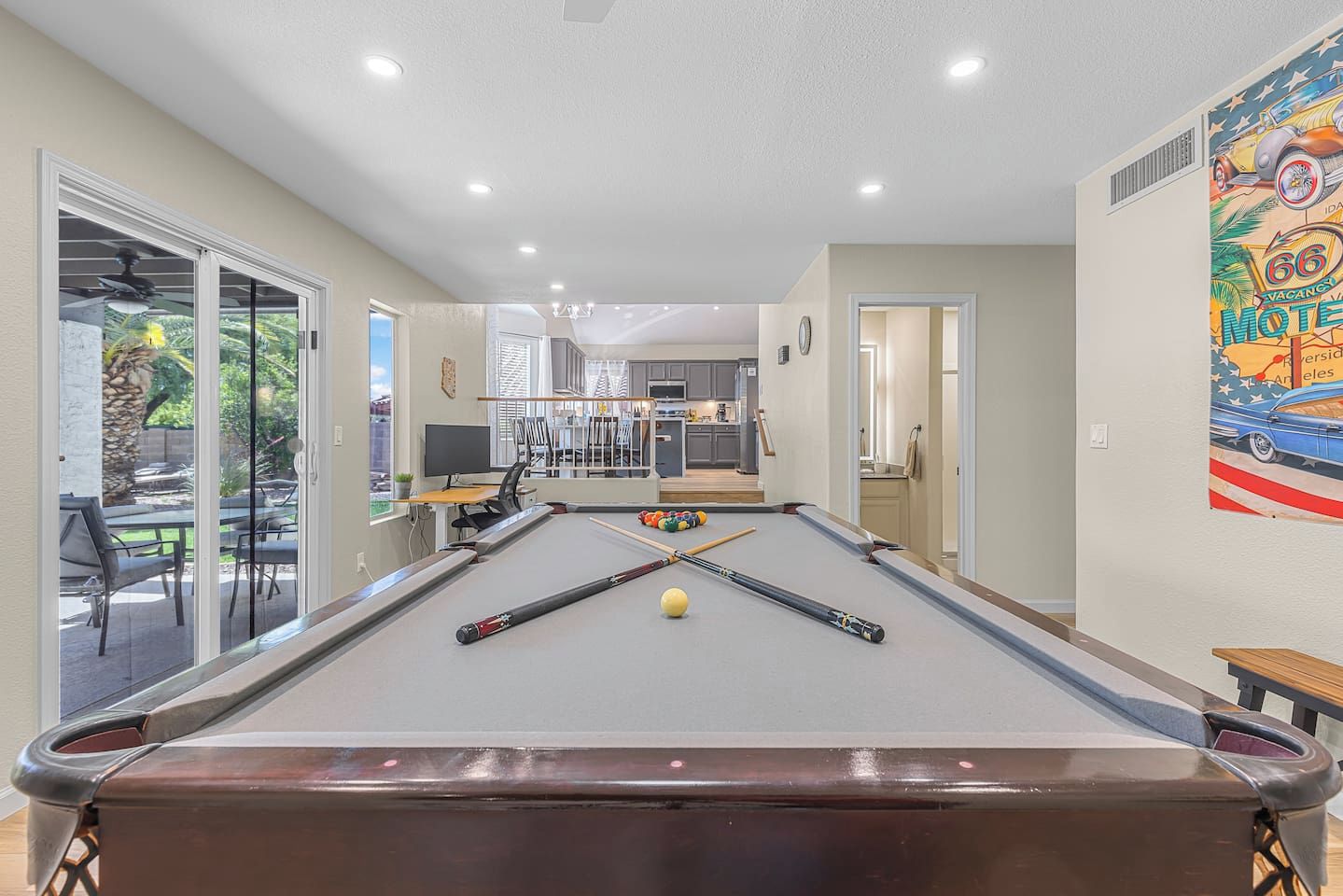 A pool table in a room with a view of a patio area, a dining table, and a kitchen in the background.