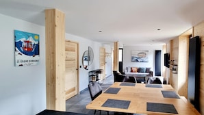 Ein moderner Essbereich mit einem Holztisch und Stühlen, einer Couch und einem an der Wand montierten Fernseher.