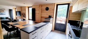 A modern kitchen with a central island, wooden walls, and a view of a forested area. - 2nd floor, balcony, parking, tv, ski locker, 82m², Le Grand Bornand (Le Grand-Bornand)