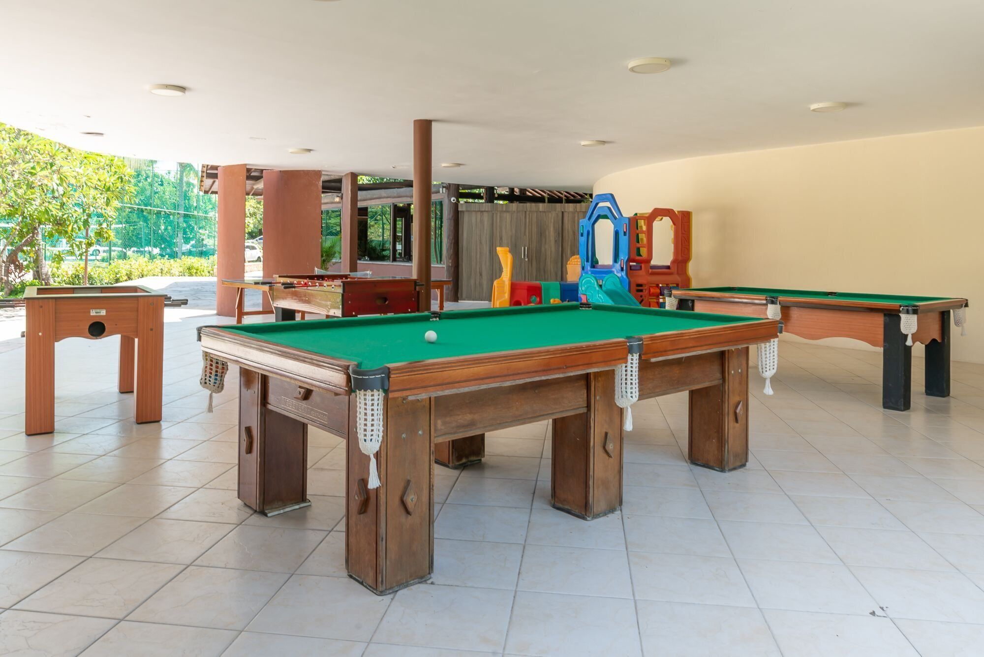 A pool table with a green felt surface, surrounded by wooden furniture and a large mirror.