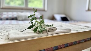 Una cama bien hecha con una toalla doblada y un pequeño detalle de follaje sobre un edredón estampado.