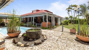 A house with a pool, surrounded by potted plants and a stone pathway.