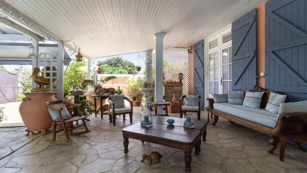 A covered patio area with stone flooring, wooden furniture, and potted plants.
