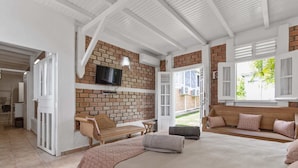 A spacious room with a large bed, a television mounted on a brick wall, and a view of the outdoors through a window.