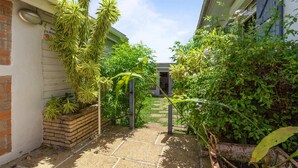 A narrow garden path leading to a house with a brick wall and a wooden fence.