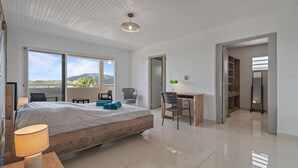 Une chambre moderne avec un grand lit, un bureau et une chaise. De grandes fenêtres offrent une vue sur l’extérieur.