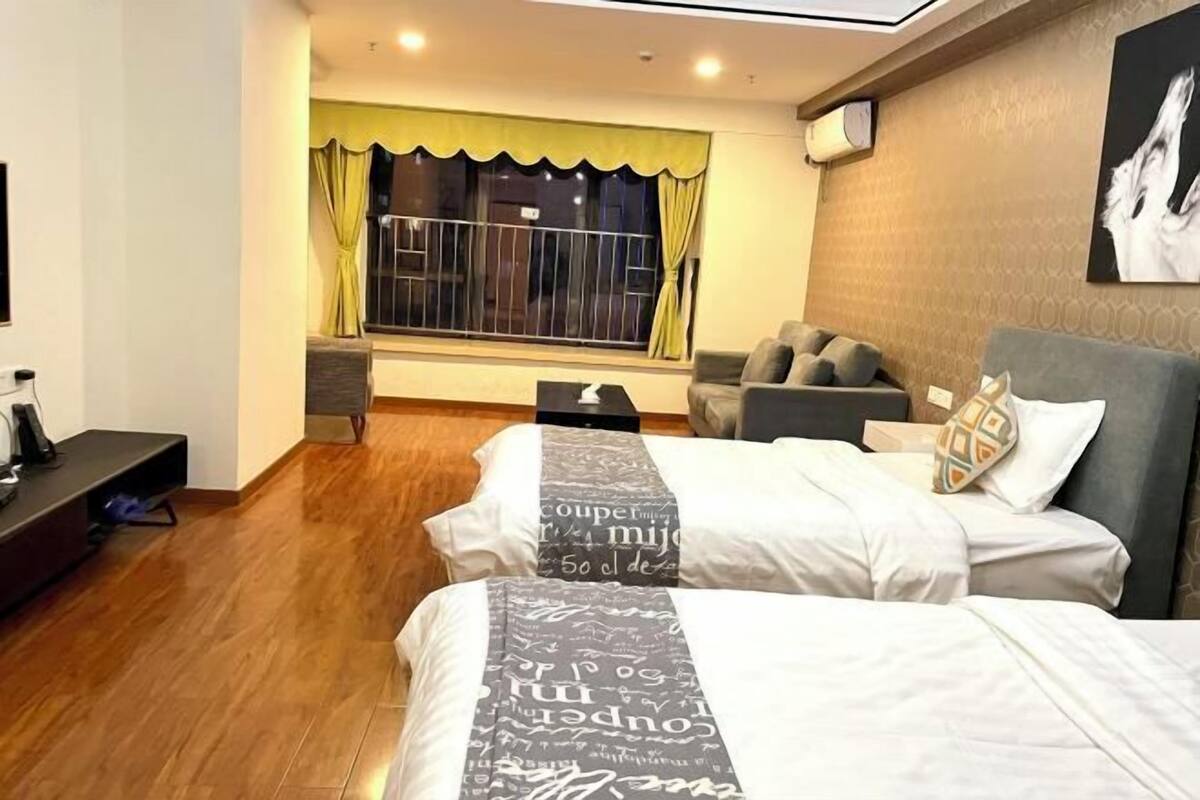A hotel room with two beds, a sofa, a TV, and a window with curtains.