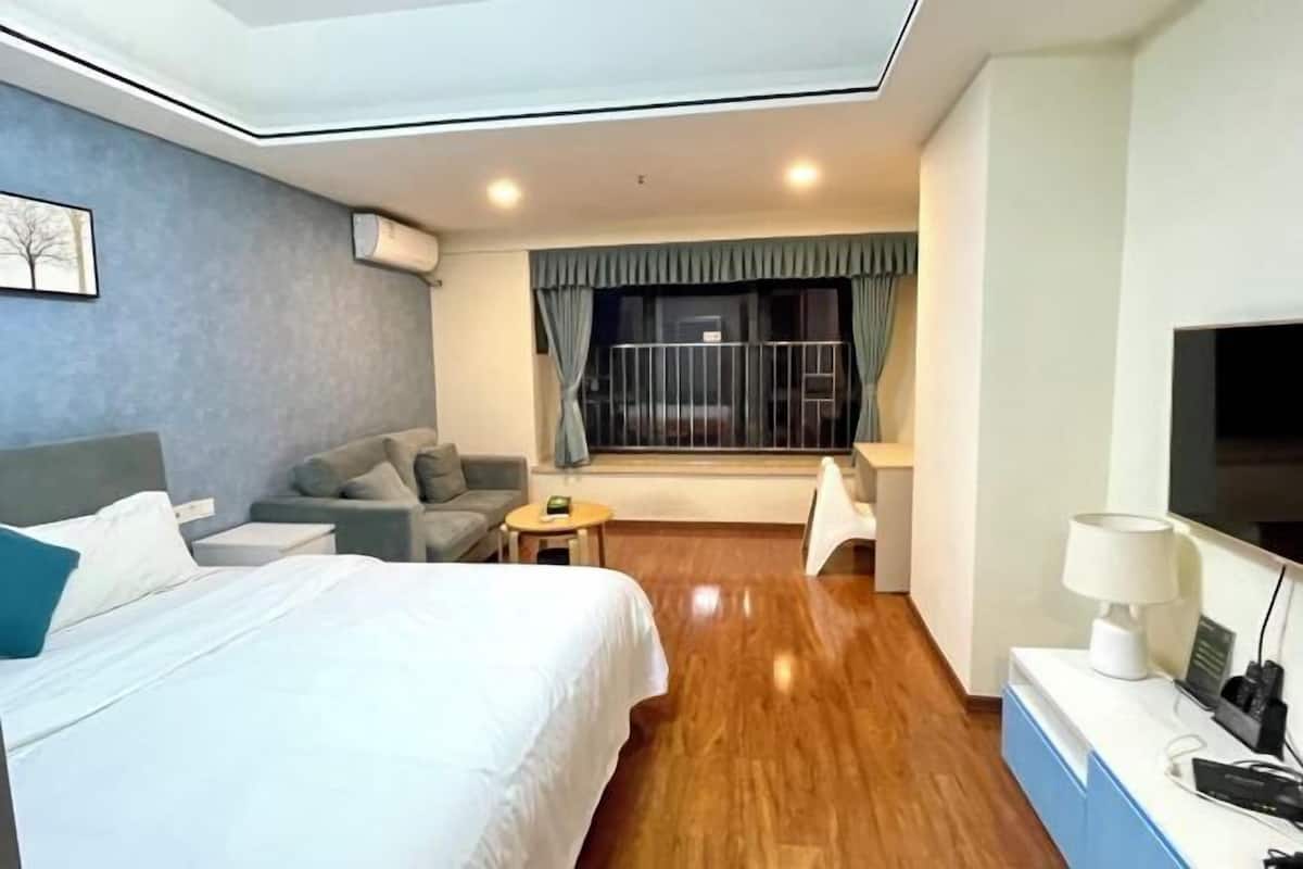 A hotel room with a bed, a sofa, a small table, a TV, and a window with curtains.