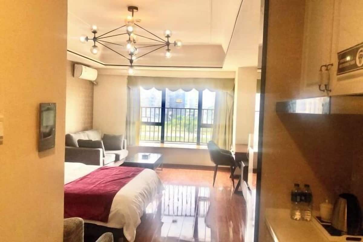 A hotel room with a bed, a desk, a chair, a sofa, a chandelier, and a view of the outdoors.
