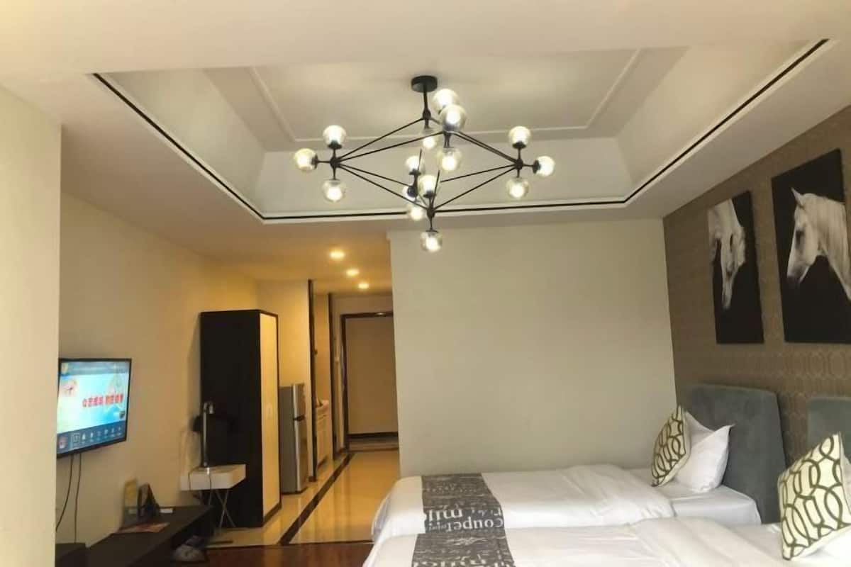 A hotel room with a modern chandelier, a bed with patterned bedding, a flat-screen TV, and artwork on the wall.
