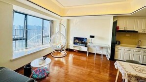 Een moderne woonkamer met een groot raam, een hangstoel, een flatscreen televisie en een keukenhoek.