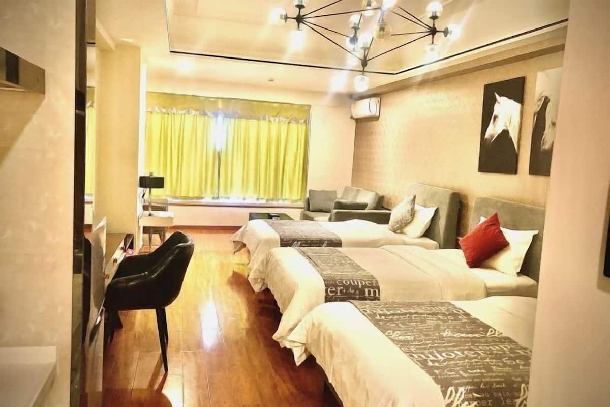 A hotel room with two beds, a desk, and a chair. There is a window with yellow curtains and artwork on the wall.