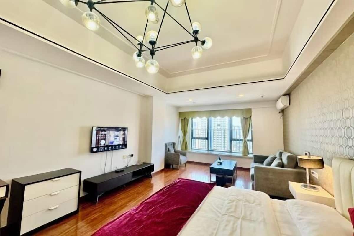 A modern hotel room with a large bed, a TV, a desk, a chair, and a sofa.