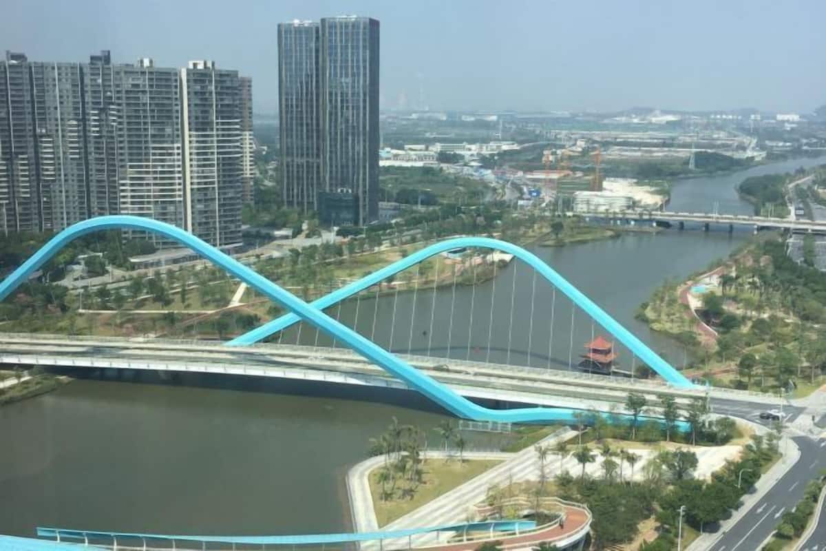 A bridge with a blue arch over a river, surrounded by high-rise buildings and greenery.