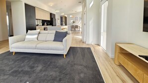 Ein modernes Wohnzimmer mit einem grauen Sofa, einem dunkelgrauen Teppich, Holzböden und einer Holzbank.