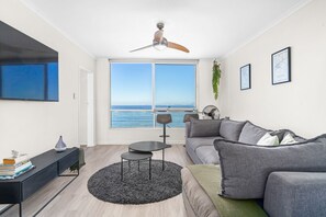 A modern living room with a large window, a ceiling fan, a grey sofa, a black coffee table, and a black rug. - Odeon Towers 808 - Two Bedroom Apartment, Sleeps 4 (Cape Town)