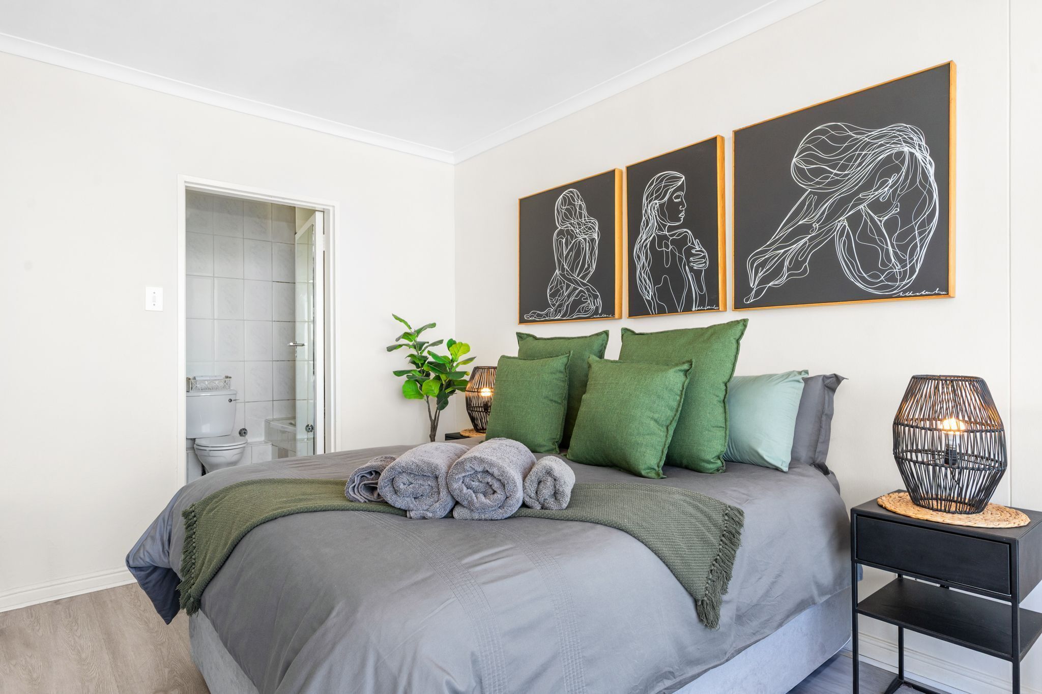 Un dormitorio moderno con una cama gris, almohadas verdes y una mesita de noche con lámpara.