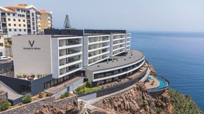 Un hôtel moderne doté d’un balcon incurvé donnant sur la mer, d’une piscine et d’une falaise rocheuse.