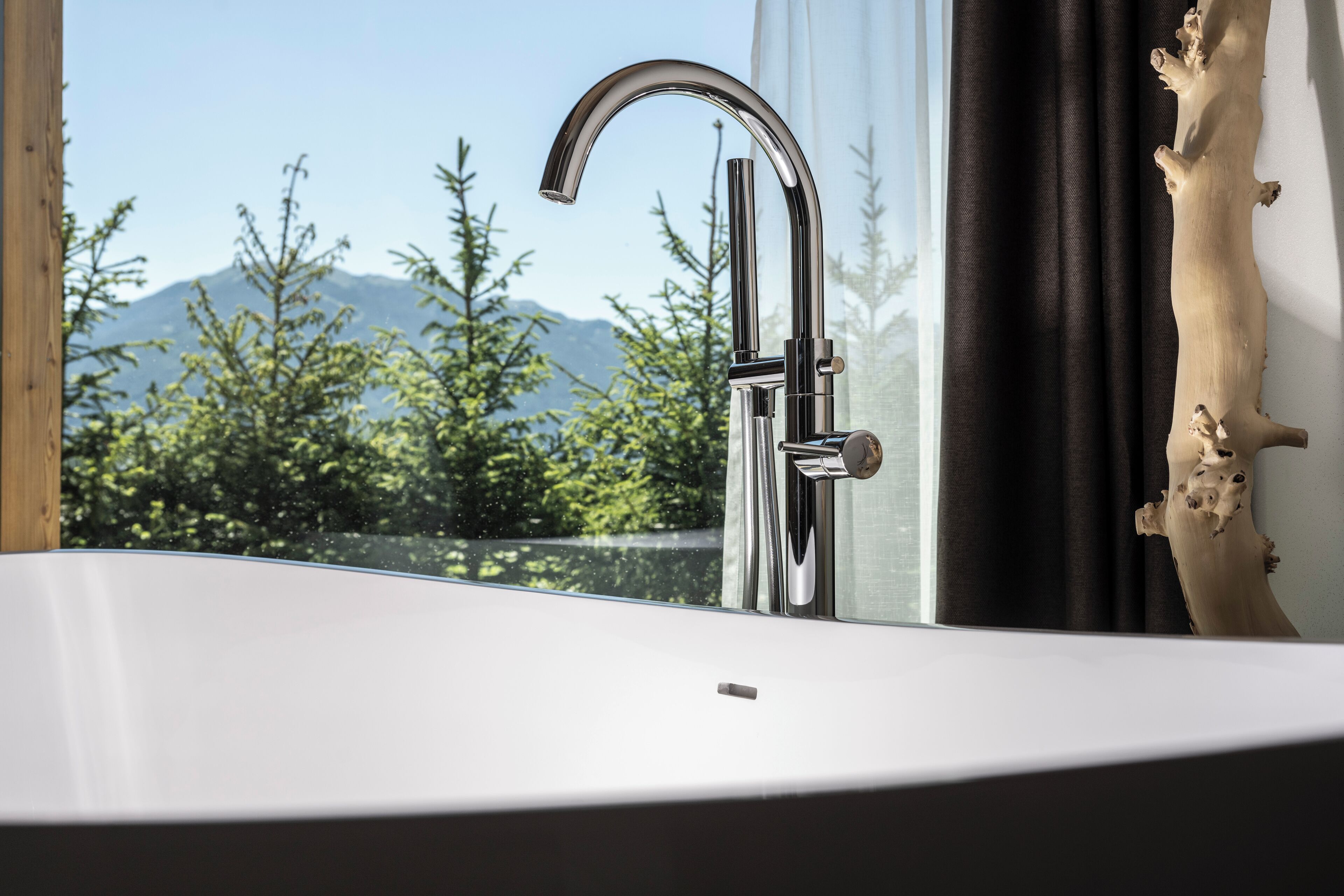 A modern bathroom with a large window, a chrome faucet, and a wooden decor piece.