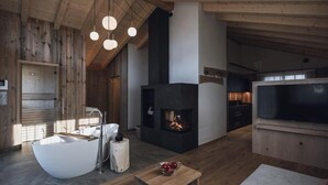 A modern living room with a large fireplace, a white bathtub, and a flat-screen TV. - Kessler's Mountain Lodge (Naz Sciaves)