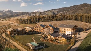 A lodge with multiple wooden cabins, a central building, and a vineyard in the background. - Kessler's Mountain Lodge (Naz Sciaves)