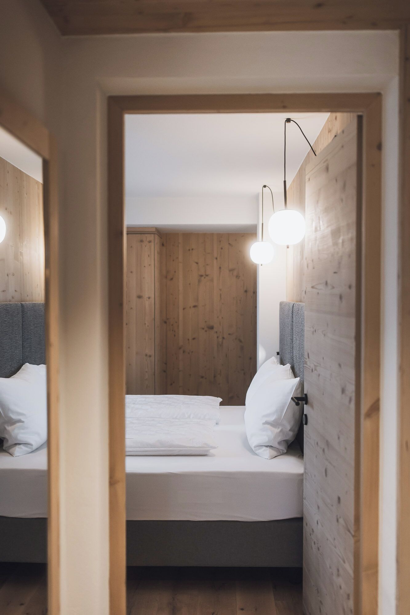 A bedroom with a wooden wall, a bed with white bedding, and a modern light fixture.