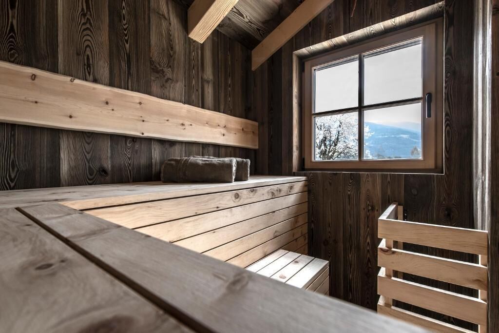 A wooden cabin interior with a bench, a window with a view, and a sloped ceiling.