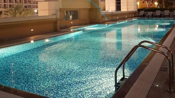 En swimmingpool med ett klart, blått vatten, omgiven av höga byggnader och en modern arkitektonisk struktur.