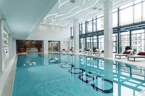 Une grande piscine intérieure dotée de chaises longues et d’un design de plafond moderne.