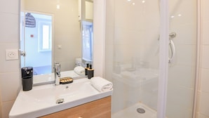 Un baño moderno con lavamanos blanco, espejo y ducha con cerramiento de vidrio.