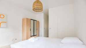 Un dormitorio moderno con una cama grande, un armario de madera y una lámpara colgante de mimbre.