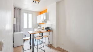 Una cocina compacta con un refrigerador pequeño, una cafetera y un ventanal con cortinas.