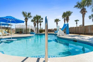 Une piscine avec un toboggan, des palmiers et une clôture en bois.