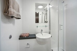Une salle de bain avec un lavabo blanc, une cabine de douche en verre, un porte-serviettes et un miroir.